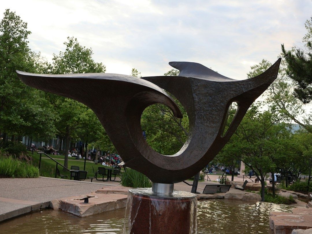 Stor moderne metalskulptur ved et lavt bassin i en grøn park