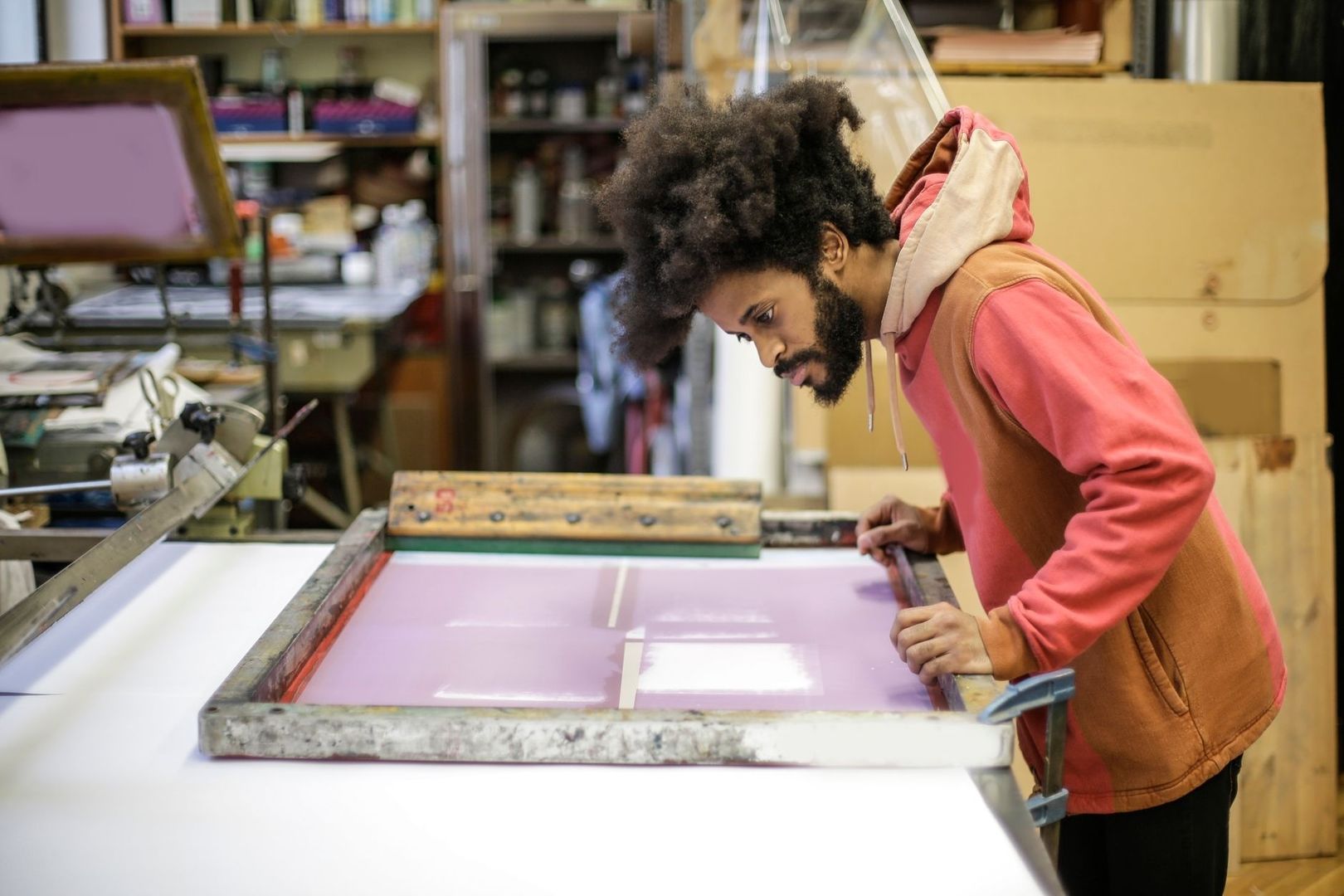 Person arbejder med serigrafi-ramme og lilla trykfarve i værksted